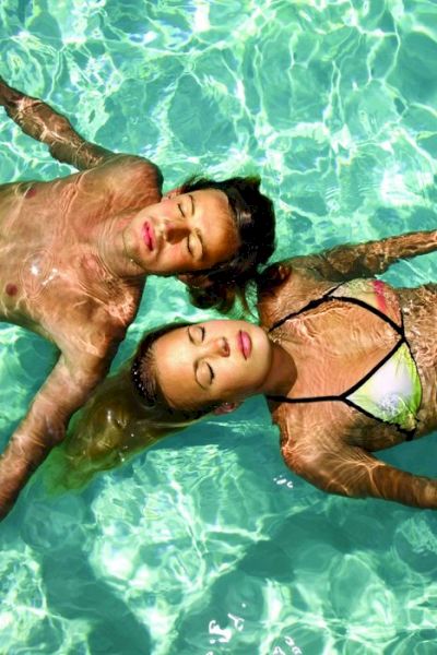 Două persoane plutesc relaxate în apa limpede a unei piscine.