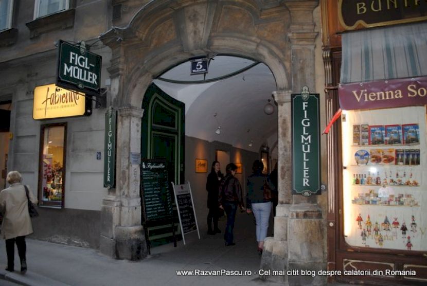 Intrare boltită de restaurant, mărginită de firme și vitrine cu meniuri.