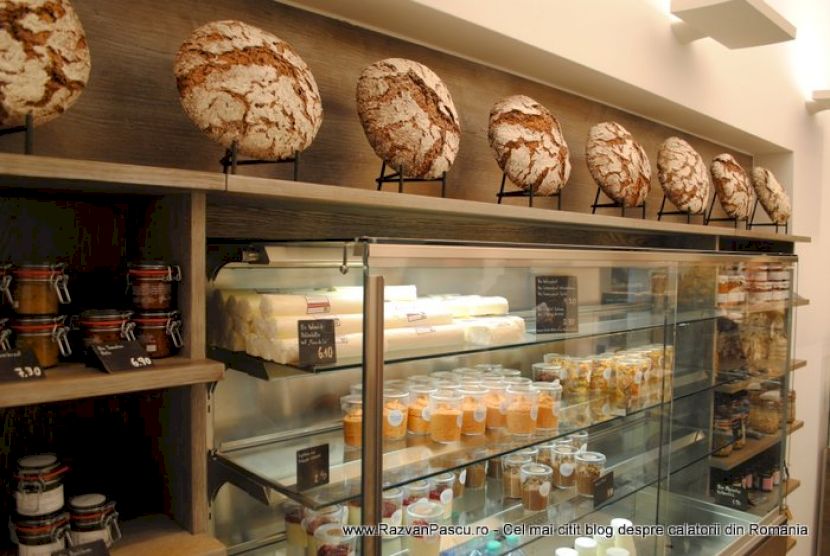 Vitrină cu produse de patiserie, sub rafturi cu pâini rotunde.