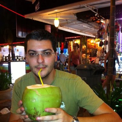 Bărbat cu ochelari bând cu paiul dintr-o nucă de cocos verde.