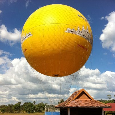 Balon galben ancorat deasupra unei construcții cu acoperiș de țiglă.