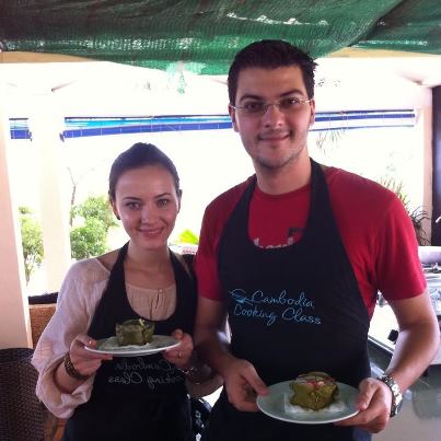 Două persoane cu șorțuri ținând farfurii cu preparate culinare.