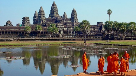 Persoane în robe portocalii lângă un bazin, cu templul Angkor Wat în fundal.