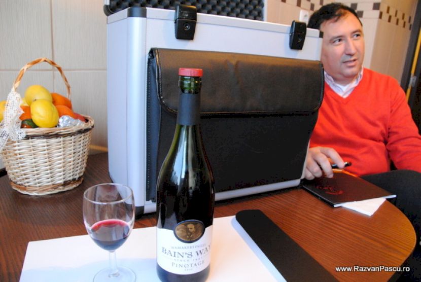 Bărbat în pulover roșu la masă cu sticlă și pahar de vin.