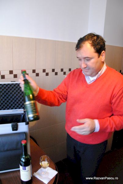 Bărbat în pulover roșu prezentând o sticlă de vin