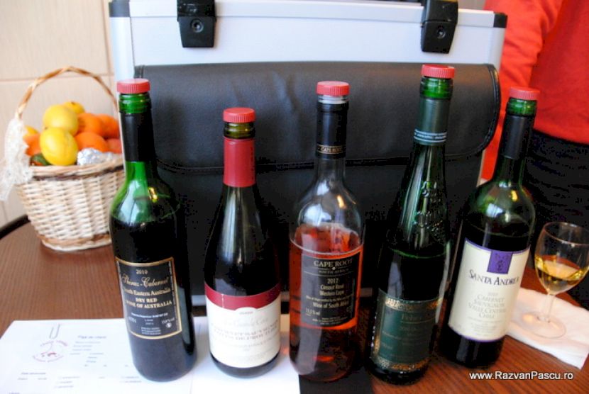Cinci sticle de vin așezate lângă un coș cu citrice