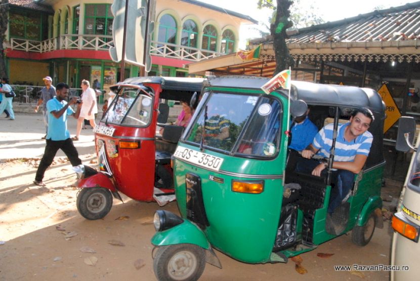 Tuk-tuk verde cu pasageri pe o stradă comercială