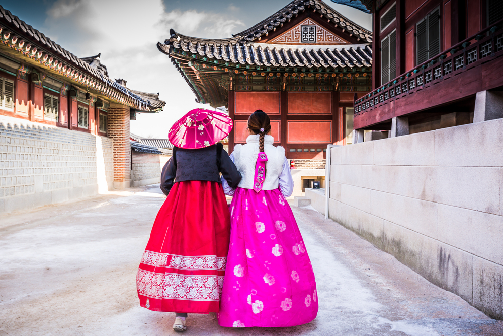 Două persoane în hanbok, pe o alee între ziduri