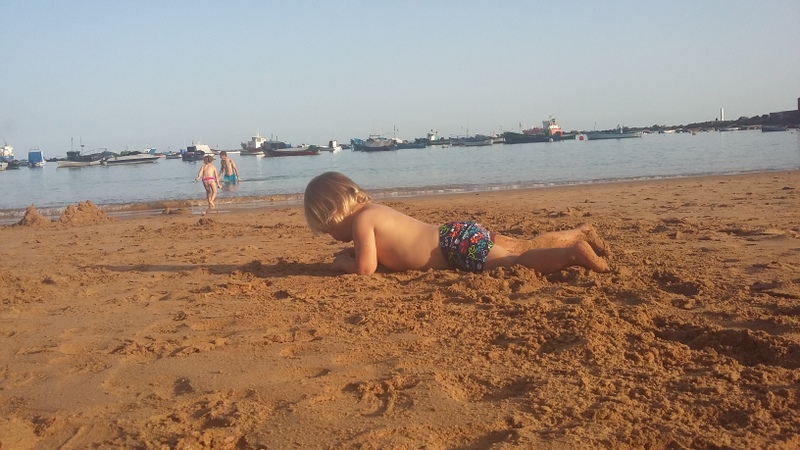 Copil pe nisip, lângă un golf liniștit