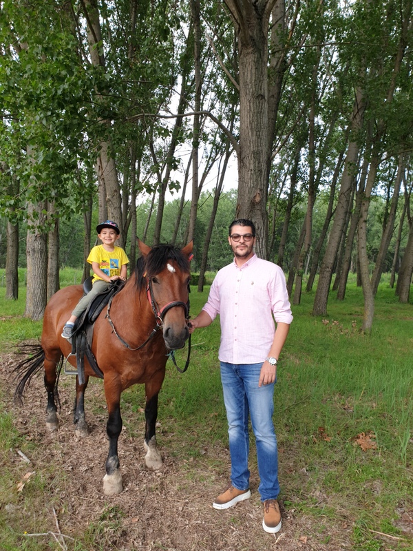 Persoană lângă un cal și călăreț între arbori
