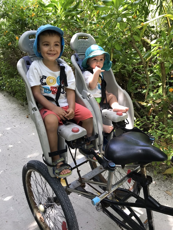 Doi copii cu căști în scaune de bicicletă