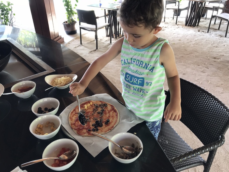 Copil lângă o masă cu pizza și boluri
