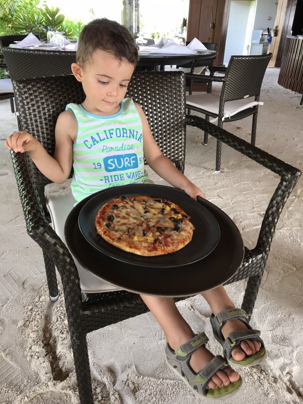 Copil ținând o tavă cu pizza lângă scaune