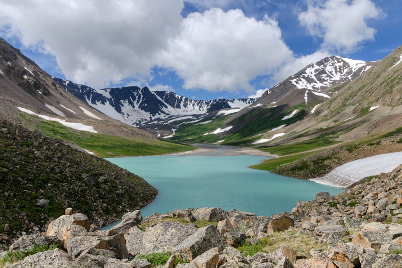 Lac turcoaz între versanți stâncoși și munți înzăpeziți