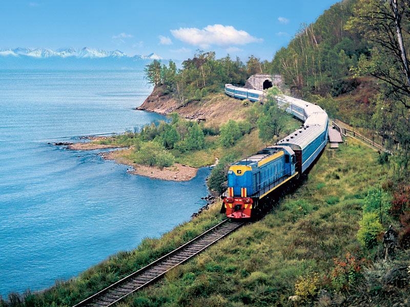 Tren cu locomotivă albastră circulând pe malul unui lac