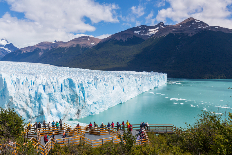 Front glaciar albastru lângă apă, între munți