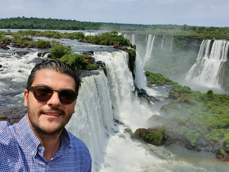 Bărbat fotografiat cu cascadele Iguazu în fundal