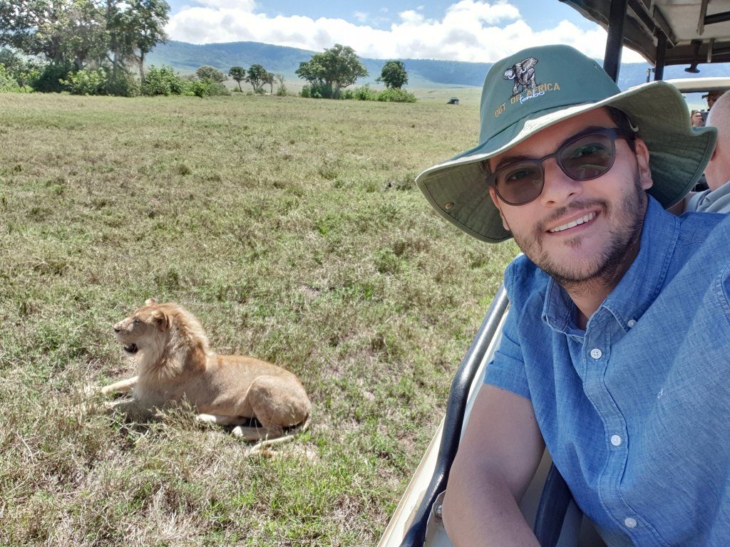 Bărbat într-un vehicul de safari, cu un leu culcat în iarbă