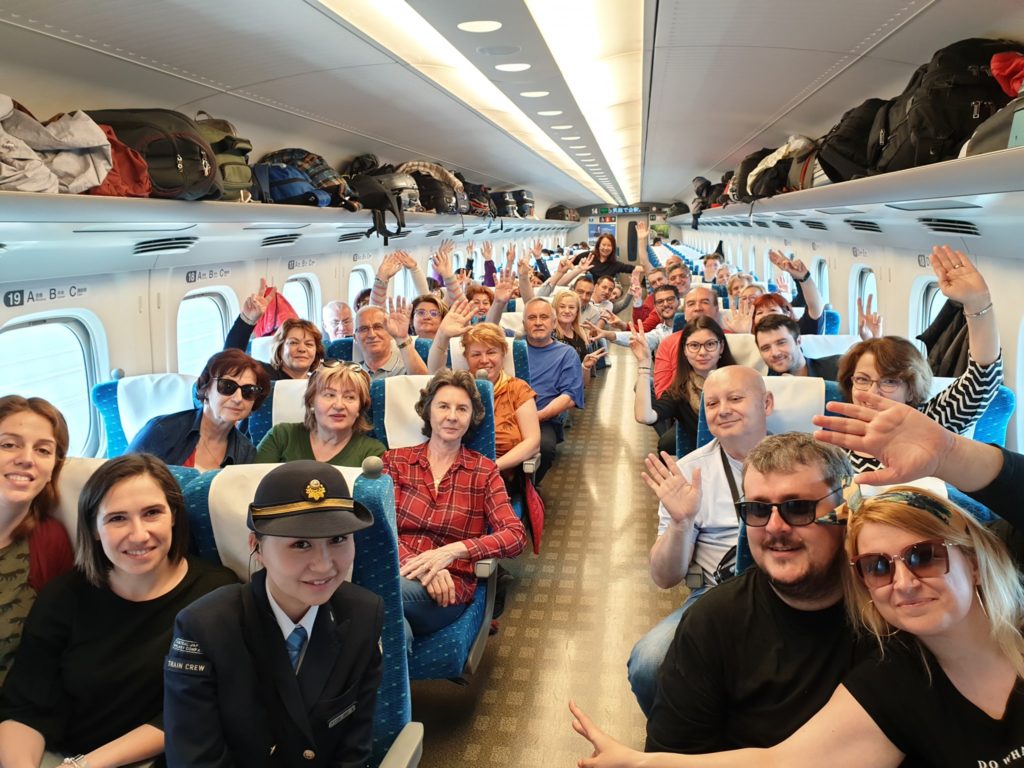 Grup de călători pozând între rândurile de scaune ale unui avion.