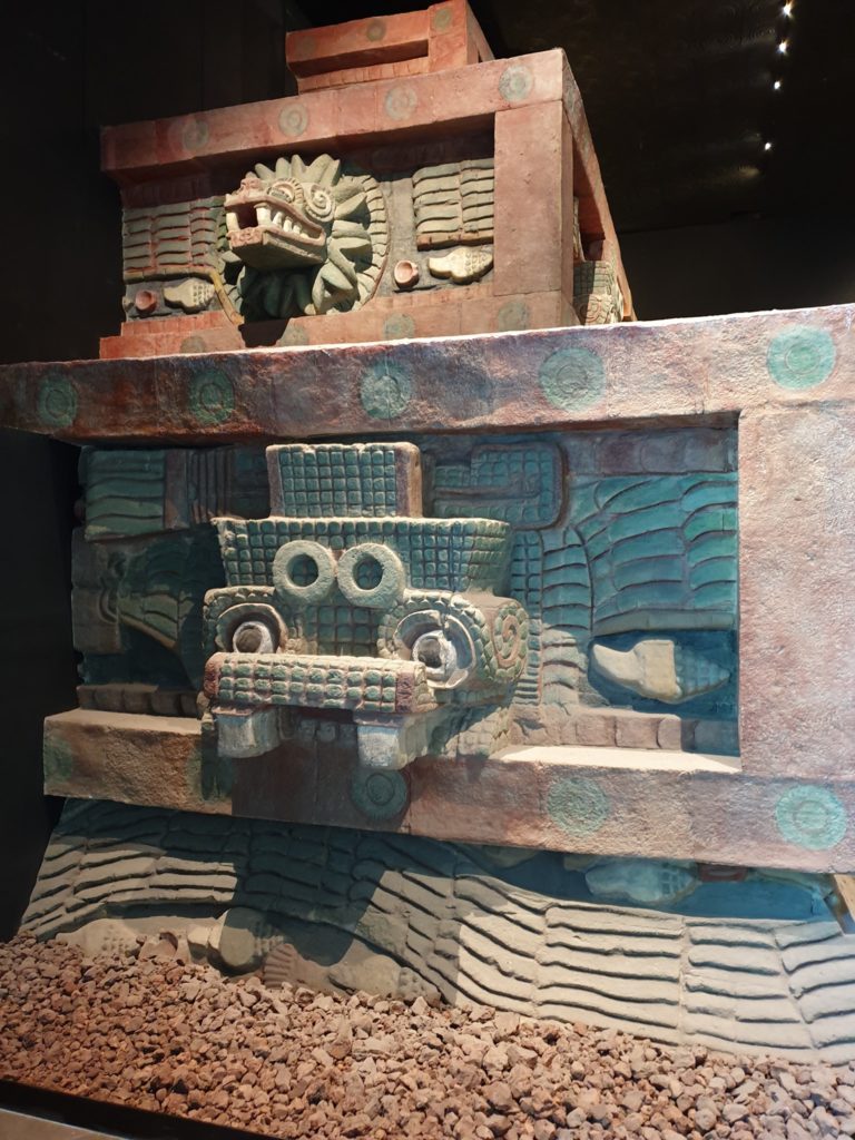 Structură expusă în muzeu, cu ornamente sculptate și fețe stilizate.