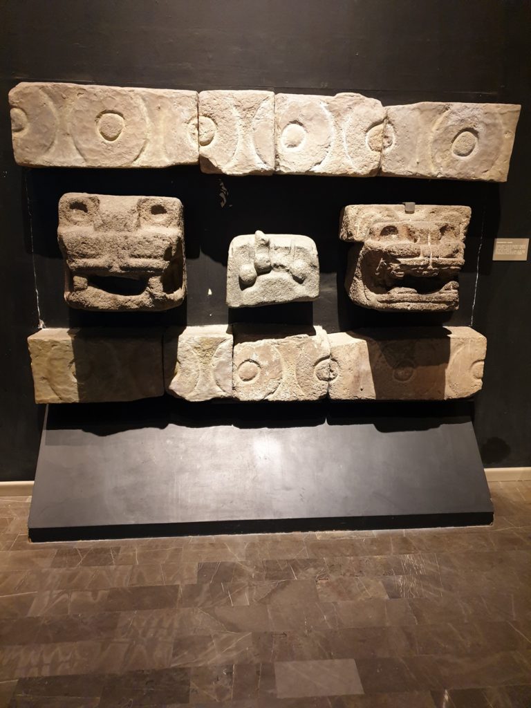 Relief din piatră cu trei chipuri sculptate, expus pe suport.