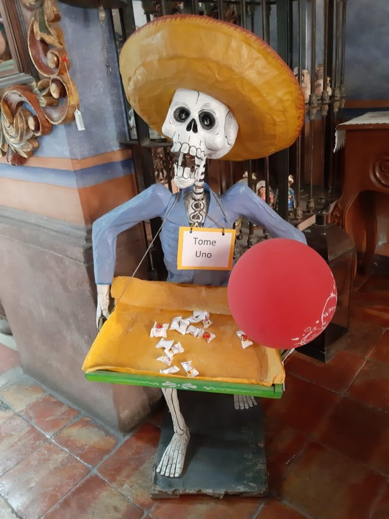 Figurină schelet cu sombrero așezată la o măsuță.