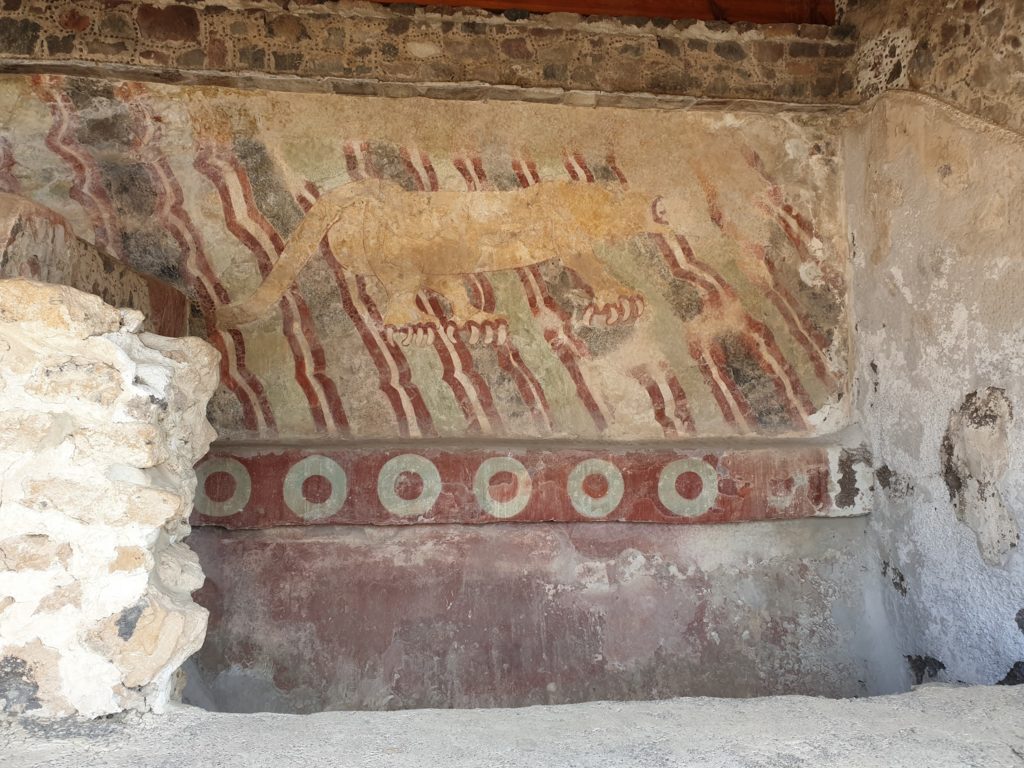 Pictură murală veche în nuanțe roșiatice, pe un perete deteriorat.