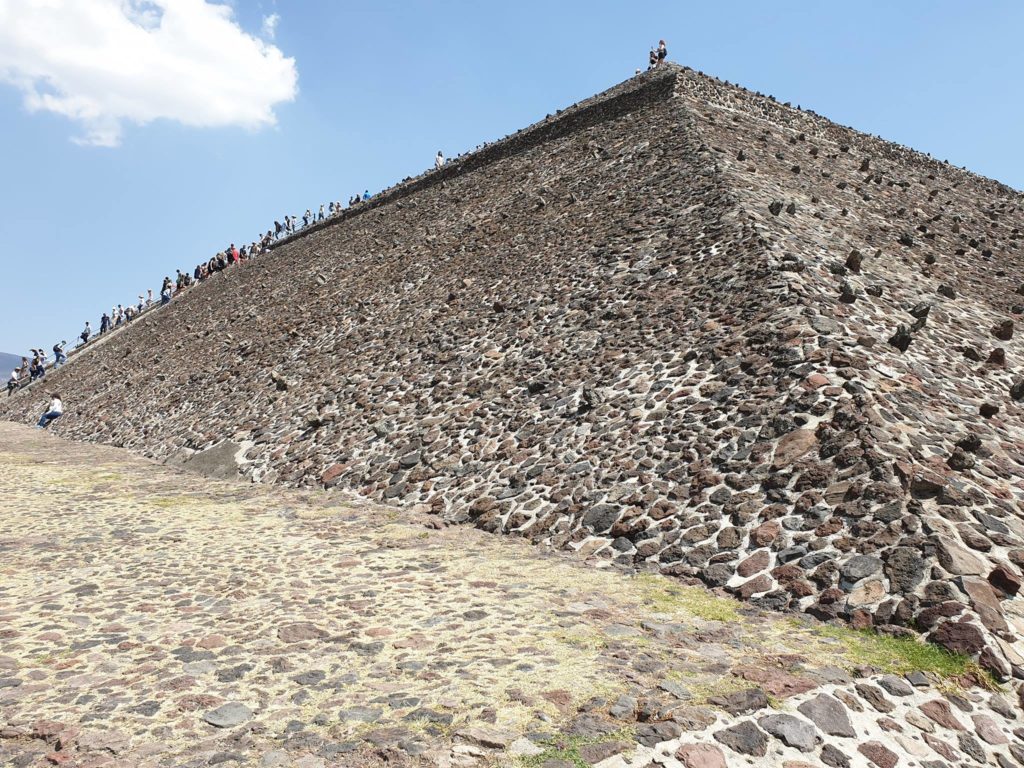 Latură înclinată a unei piramide din piatră, sub cer senin.