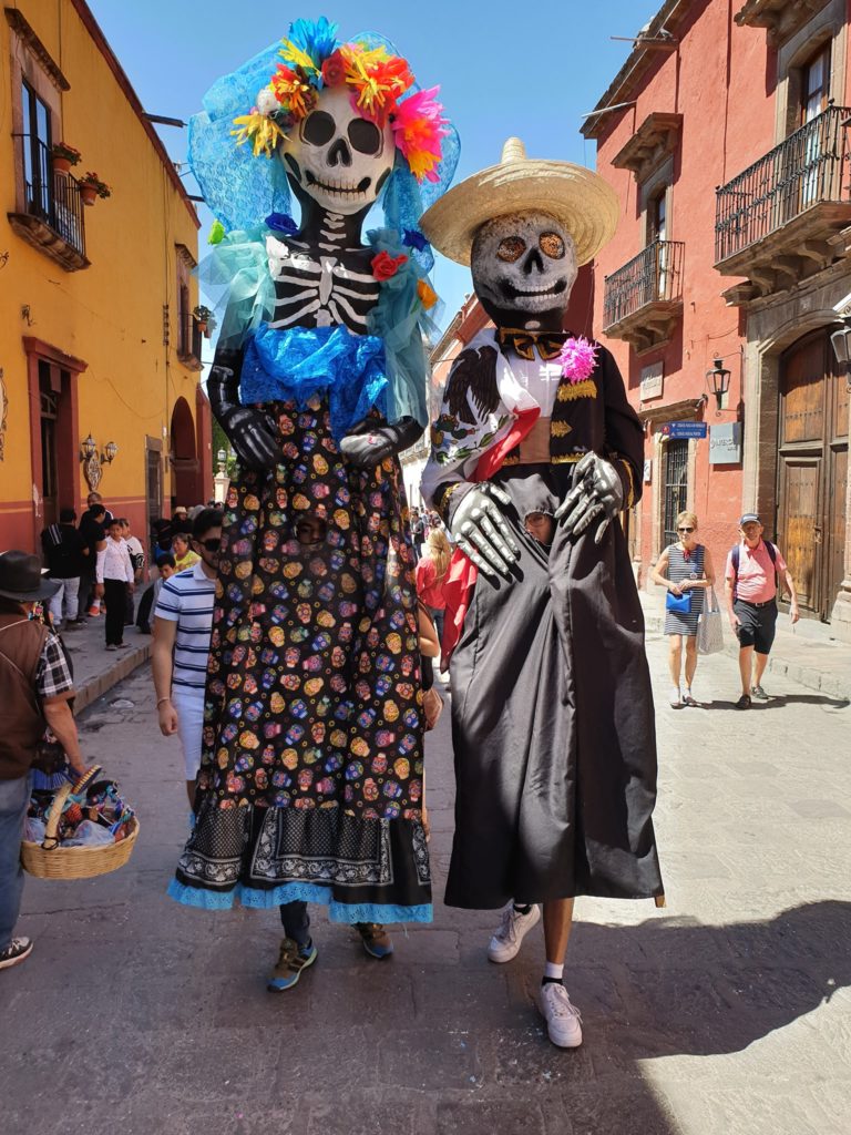 Persoane în costume decorate, pe o stradă mexicană