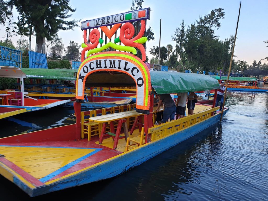 Barcă multicoloră cu acoperiș și scaune pe un canal.