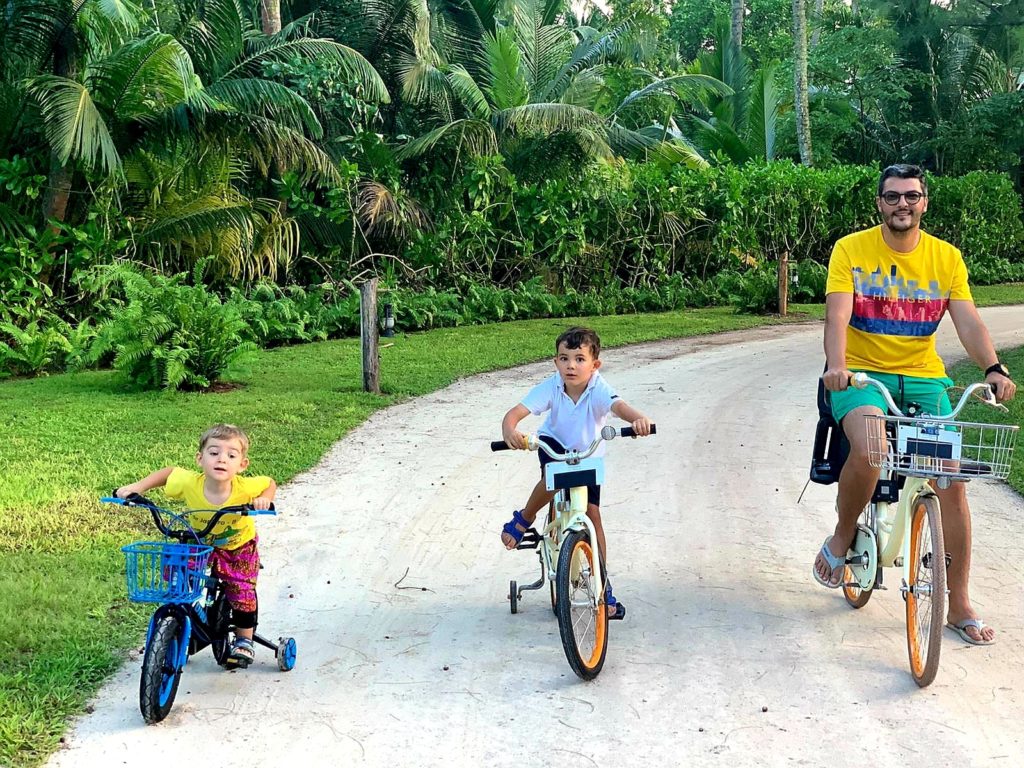 Bărbat și doi copii mergând cu bicicletele pe o alee.