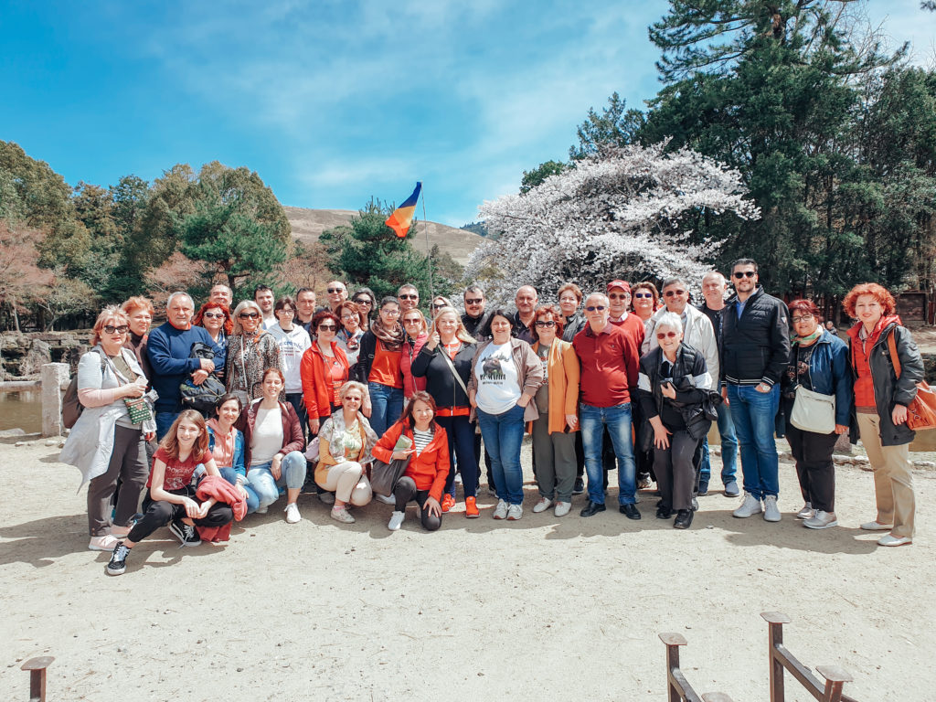 Grup de turiști pozând în fața copacilor înfloriți