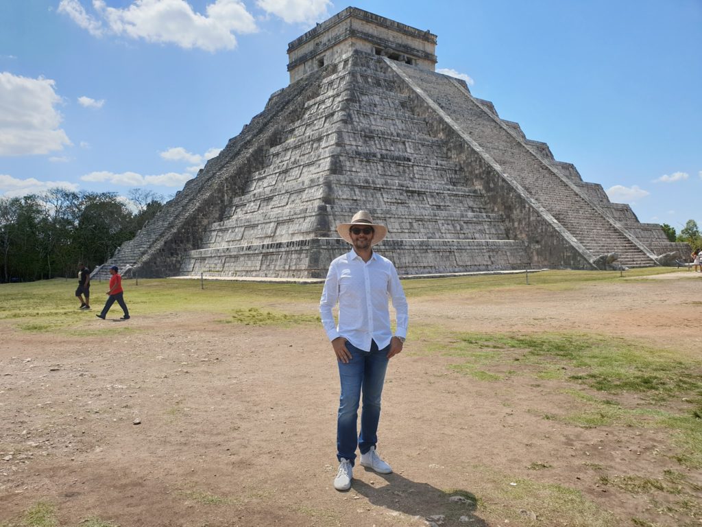 Bărbat cu pălărie în fața unei piramide din piatră.