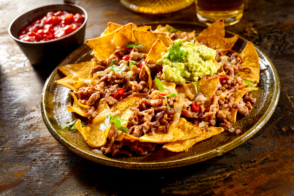 Farfurie cu chipsuri acoperite cu carne, sosuri și guacamole.