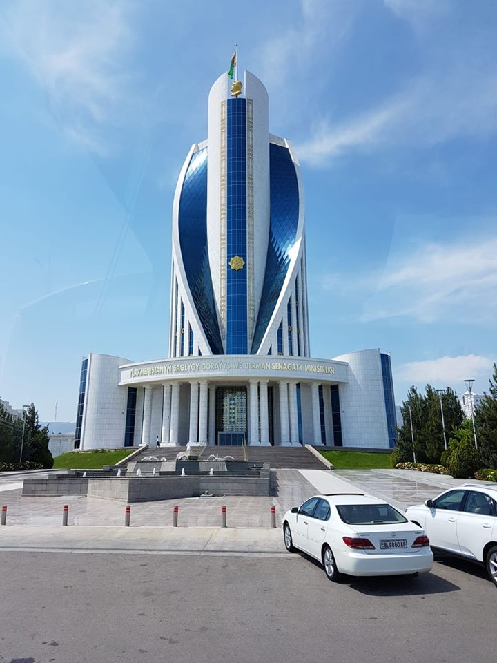 Clădire modernă albastră cu forme curbe și mașini în față