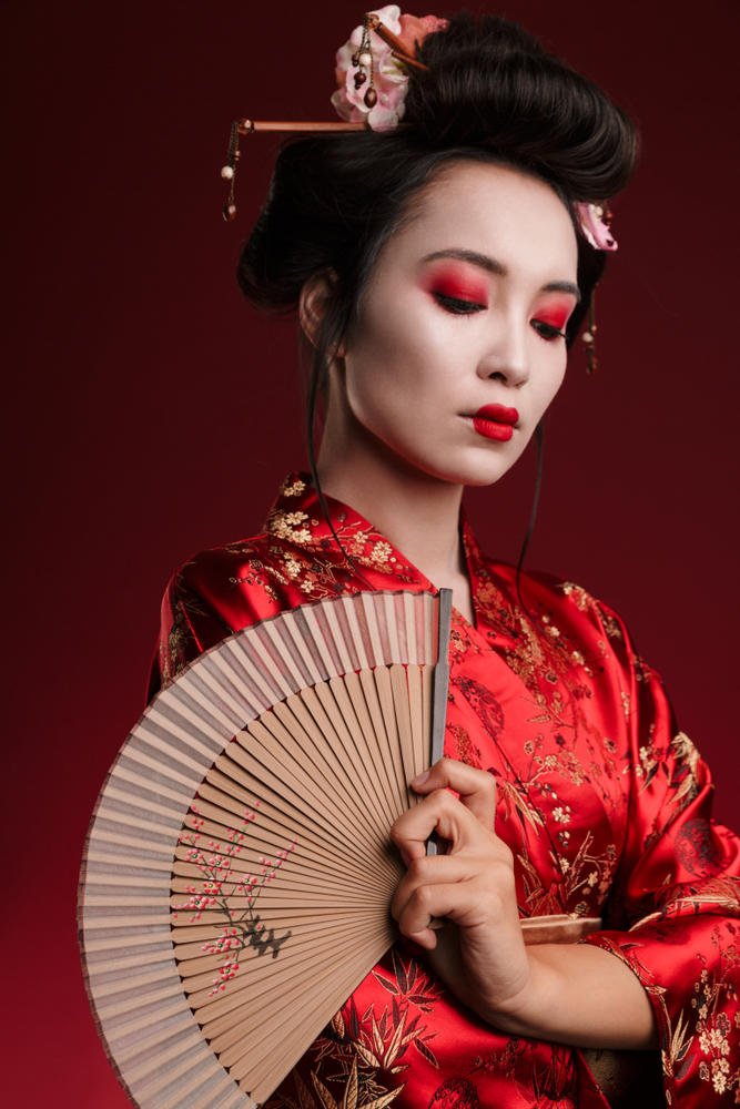Femeie în kimono roșu ținând un evantai pe fundal întunecat.