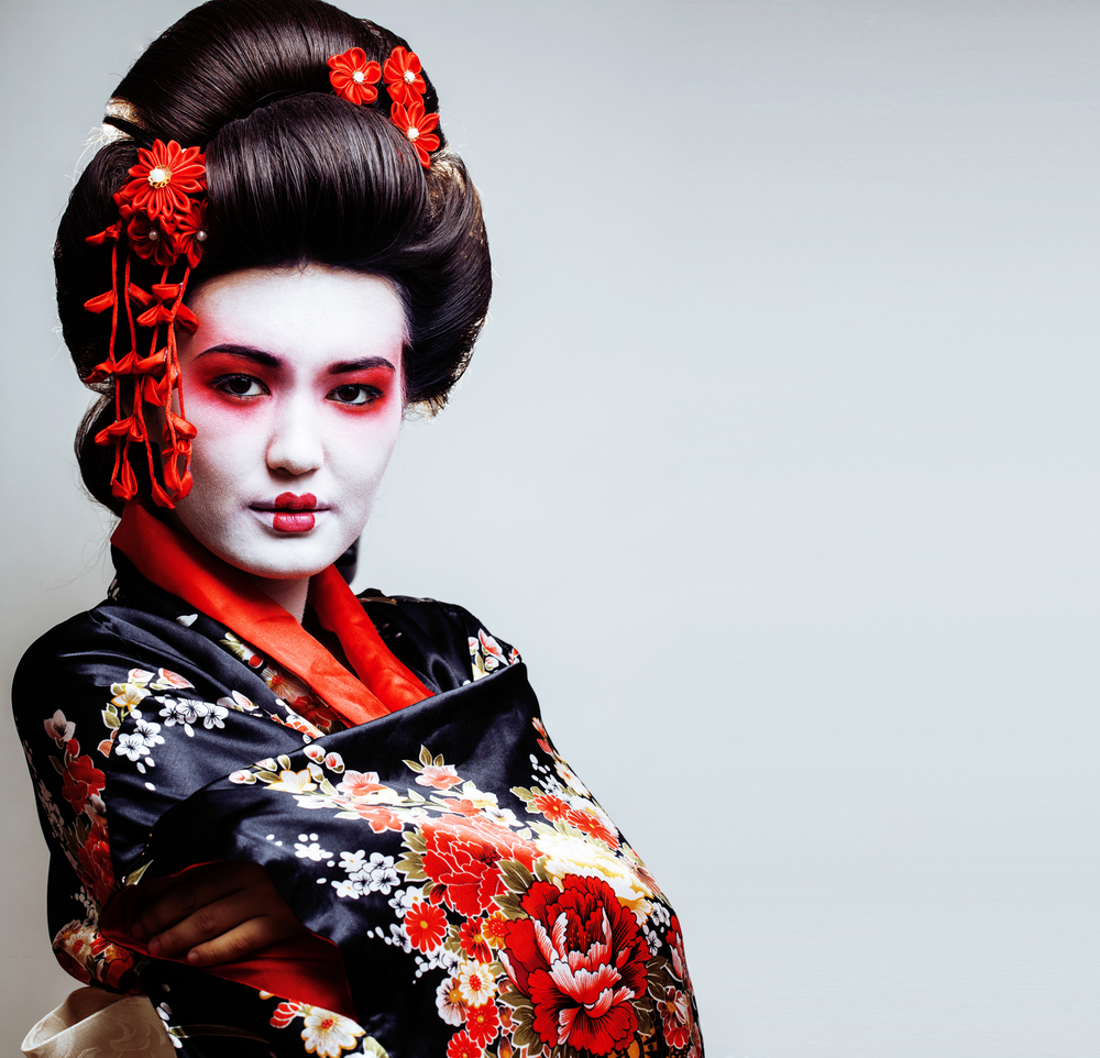 Portret de femeie cu machiaj alb, kimono negru și ornamente roșii.