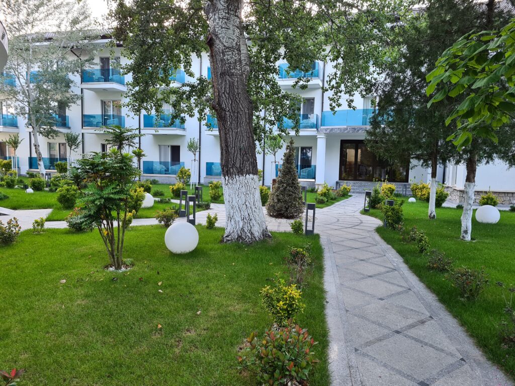 Alee pavată printre peluze și clădiri cu balcoane albastre