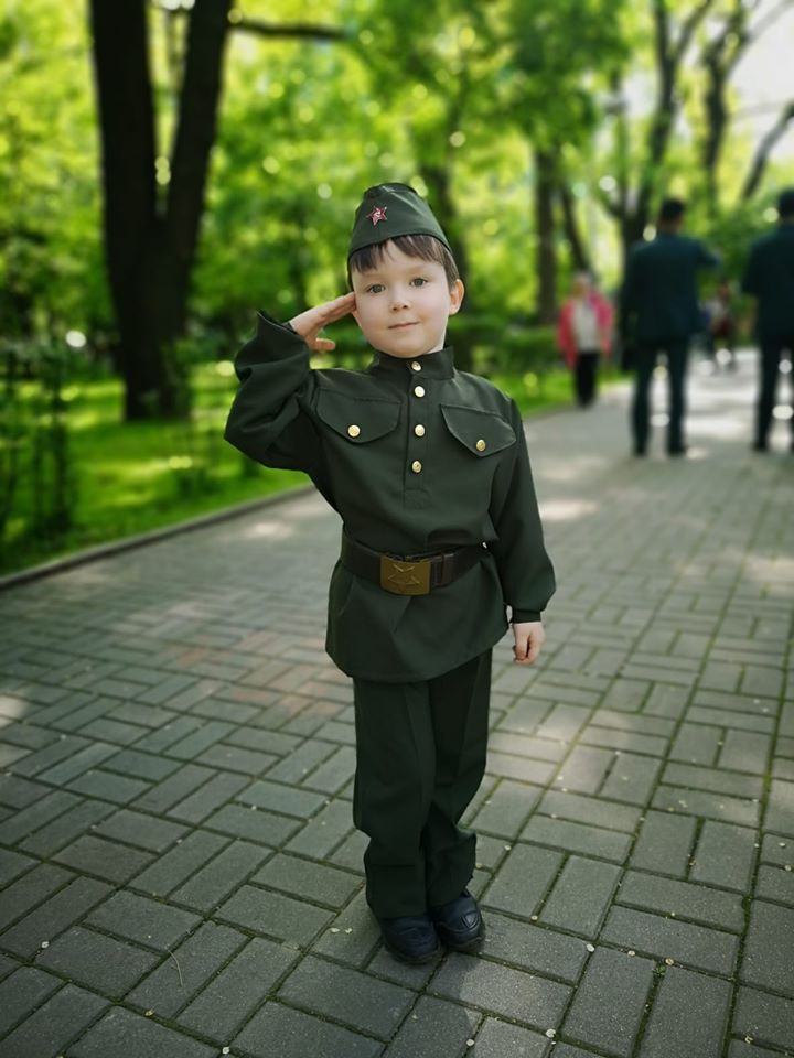 Copil în uniformă verde salutând pe o alee