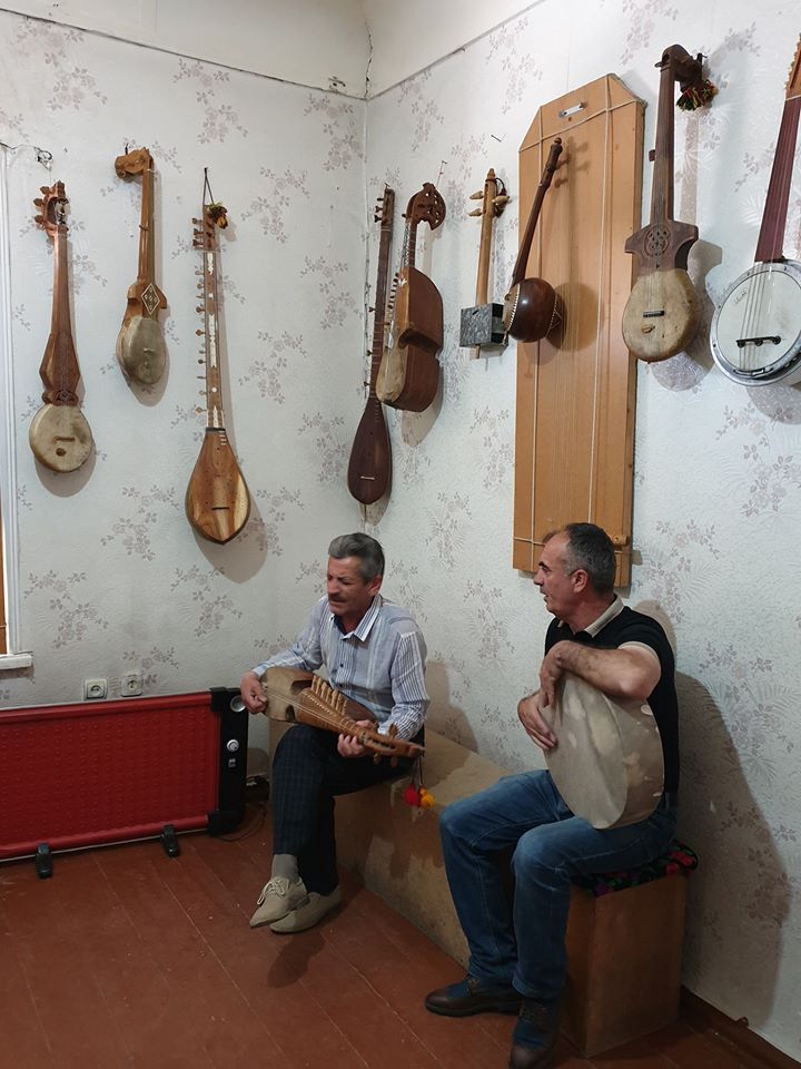 Doi bărbați cu instrumente muzicale într-o cameră cu exponate