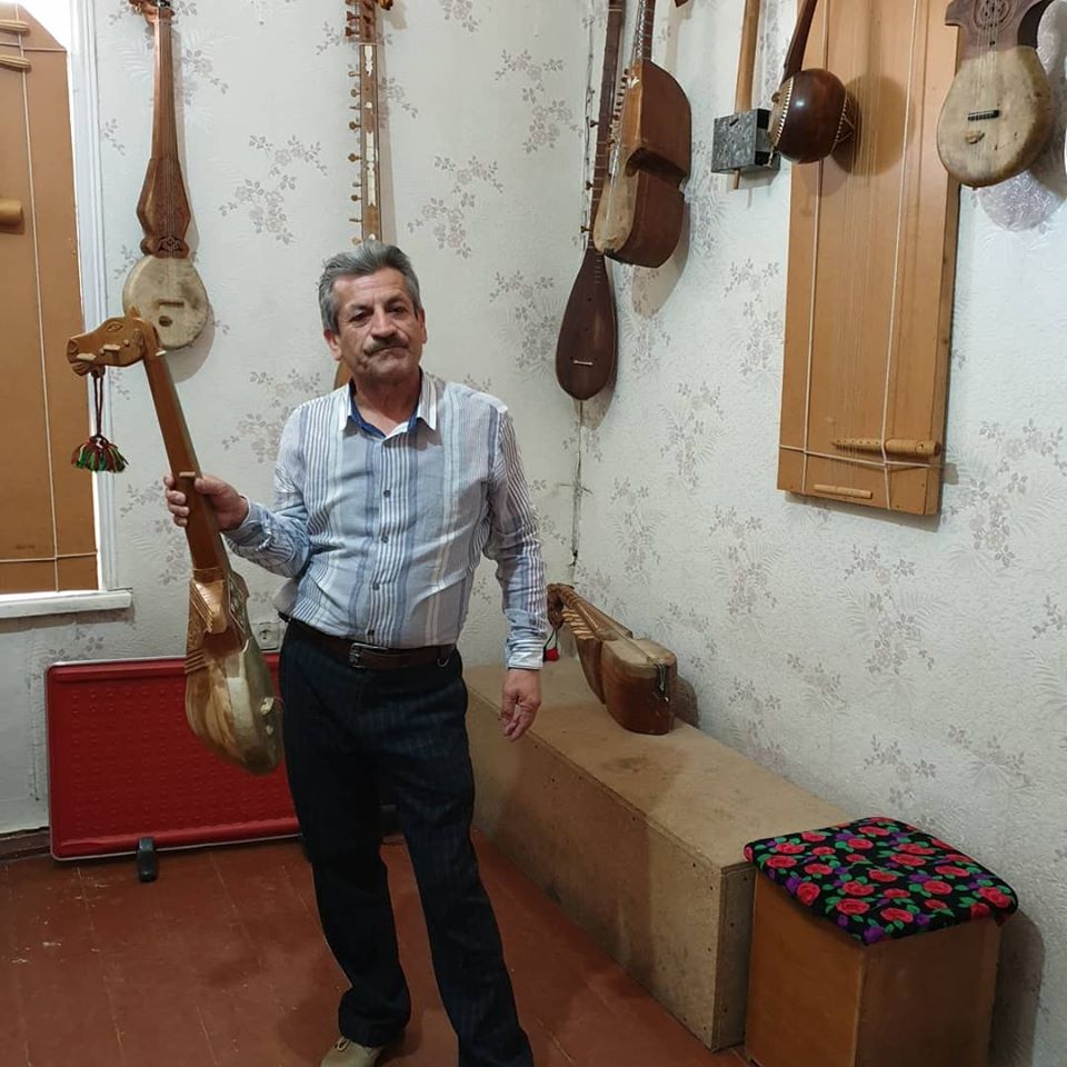 Bărbat ținând un instrument cu coarde lângă exponate muzicale