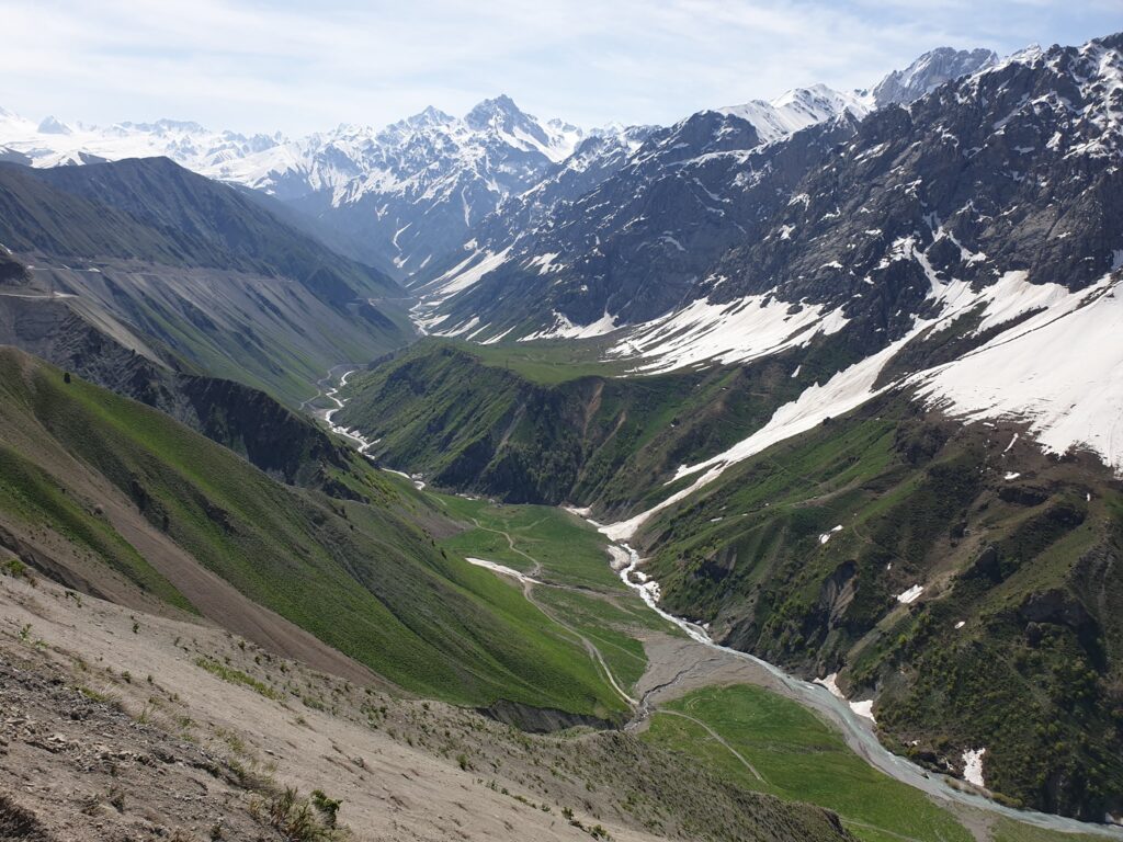 Vale montană verde între versanți cu zăpadă