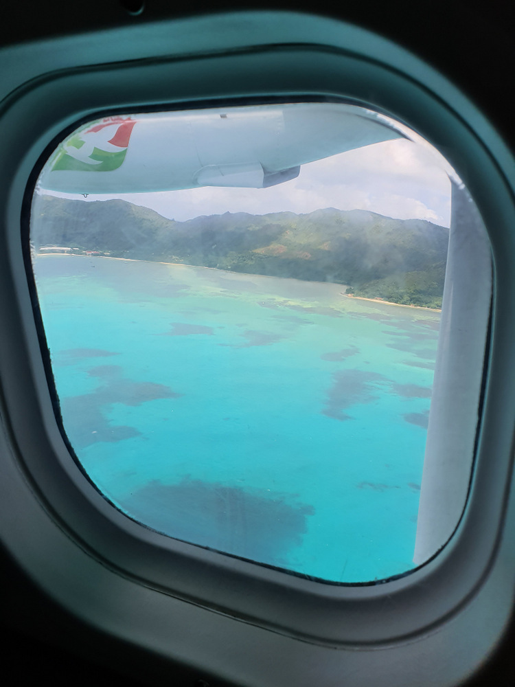 Mare turcoaz și coastă văzute prin hubloul unui avion