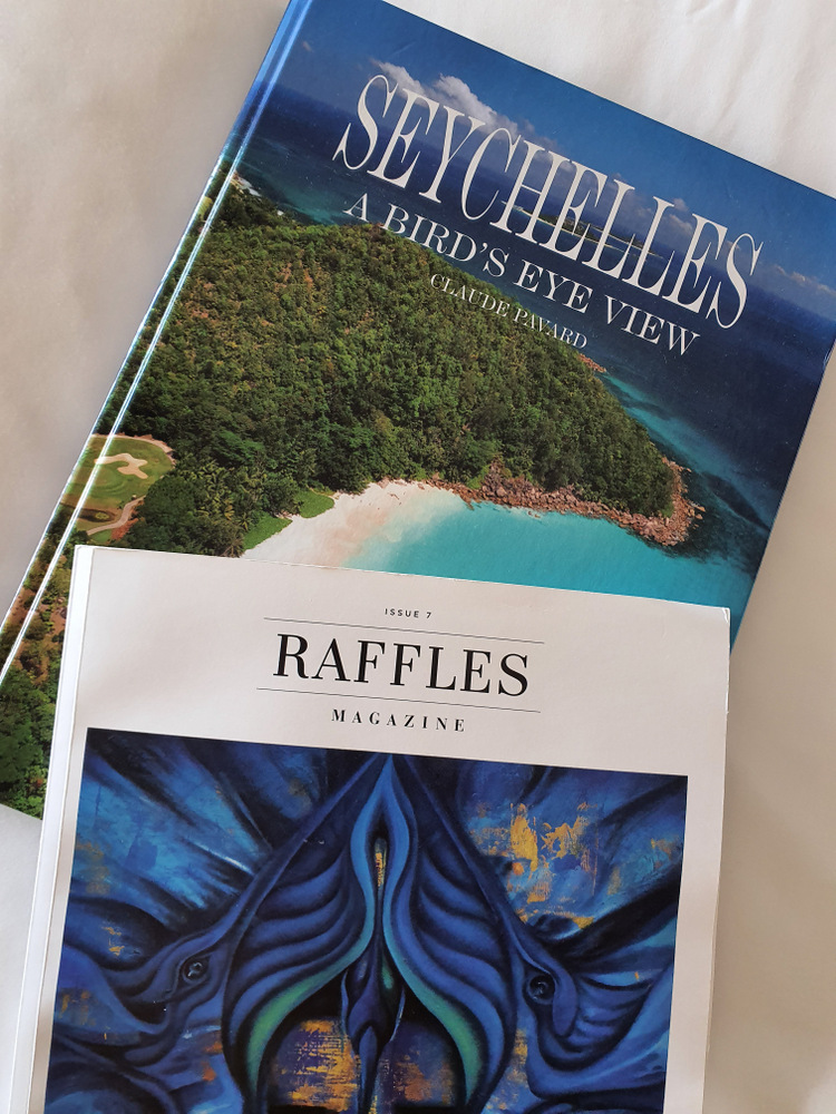 Broșuri Seychelles și Raffles așezate pe o suprafață deschisă