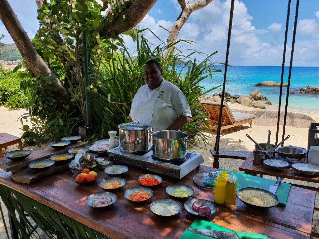 Bucătar lângă masă cu ingrediente pe o plajă tropicală