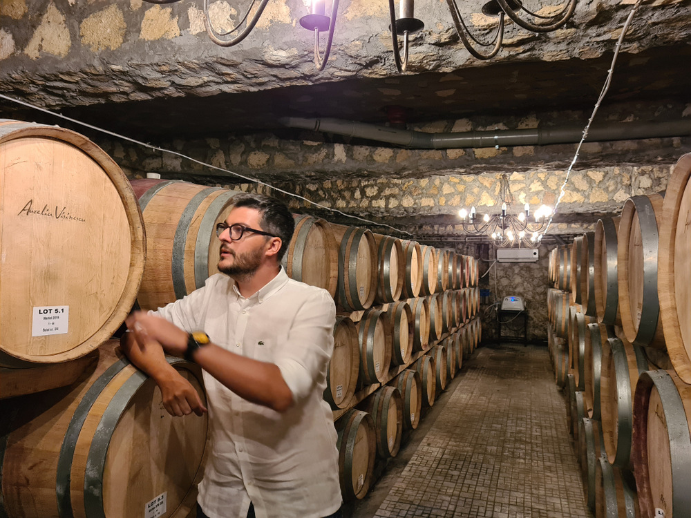Bărbat sprijinit de un butoi într-o pivniță cu vinuri