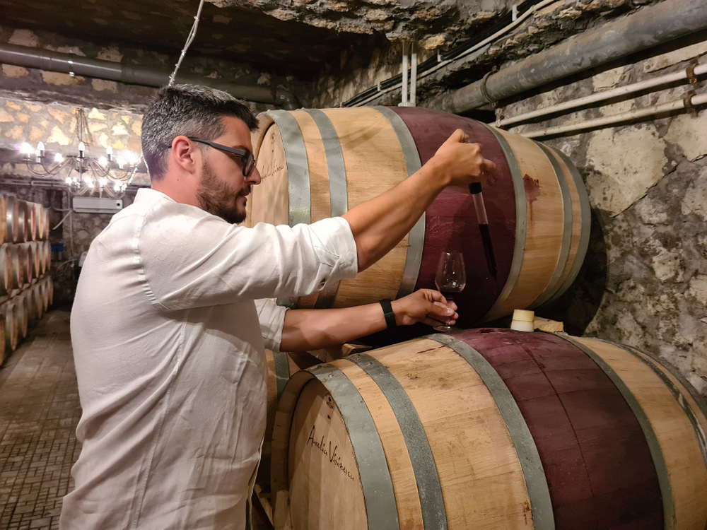 Bărbat extrăgând vin dintr-un butoi într-o pivniță
