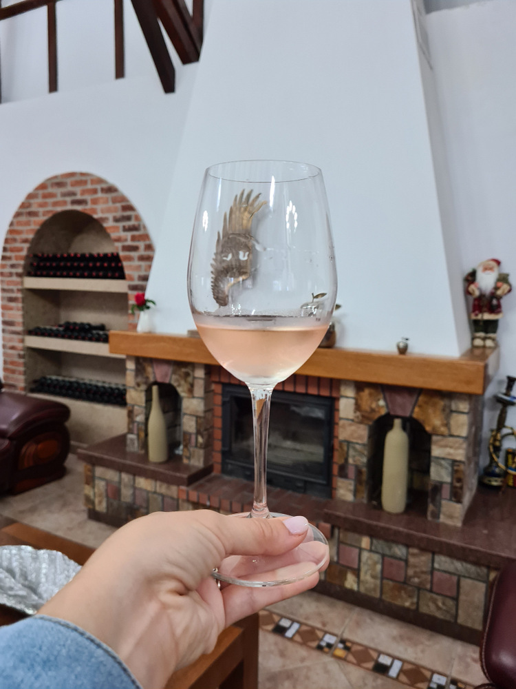 Mână ținând un pahar cu vin roze într-o sală