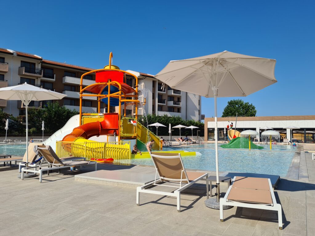 Piscină pentru copii cu tobogan galben și șezlonguri alături