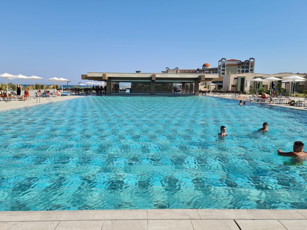 Piscină mare cu turiști și clădiri hoteliere în fundal